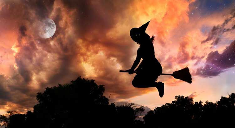 A witch on a broomstick against a dark and red sky.